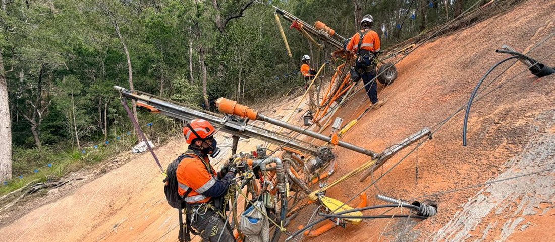 Rope access drillers installing soil nails on a steep orange rock face