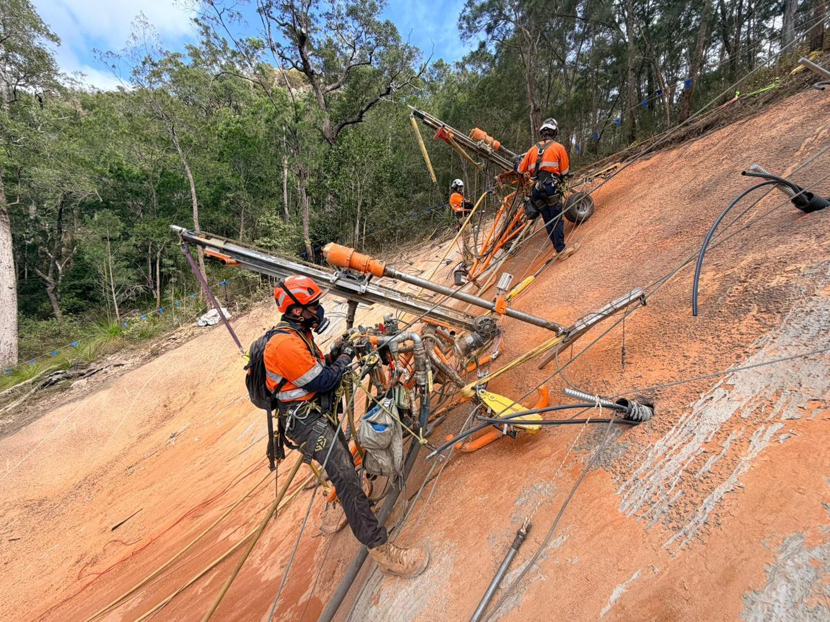 Rope access technicians rigging and drilling a slope face in daylight