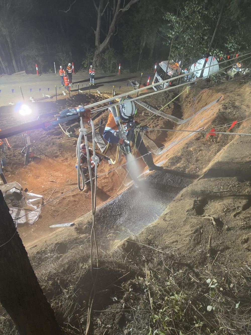 Shotcrete being applied to a slope face under lights at night